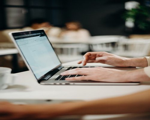 A person typing an email on a laptop while enjoying a coffee